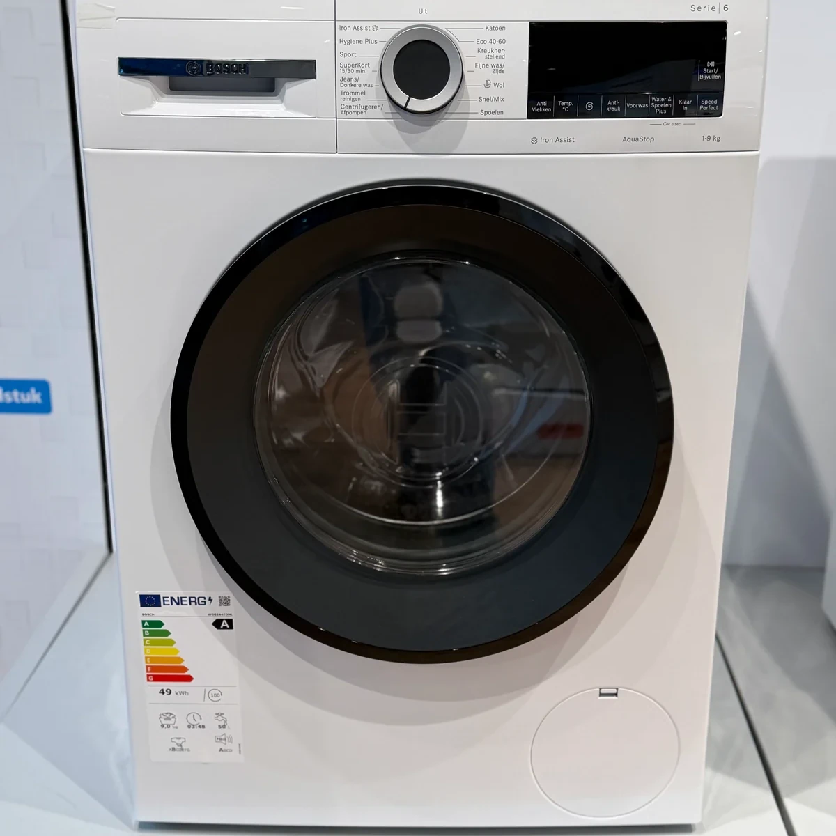 Vooraanzicht van de Bosch WGG244ZONL Iron Assist in een winkelopstelling, met gesloten deur en energielabel.