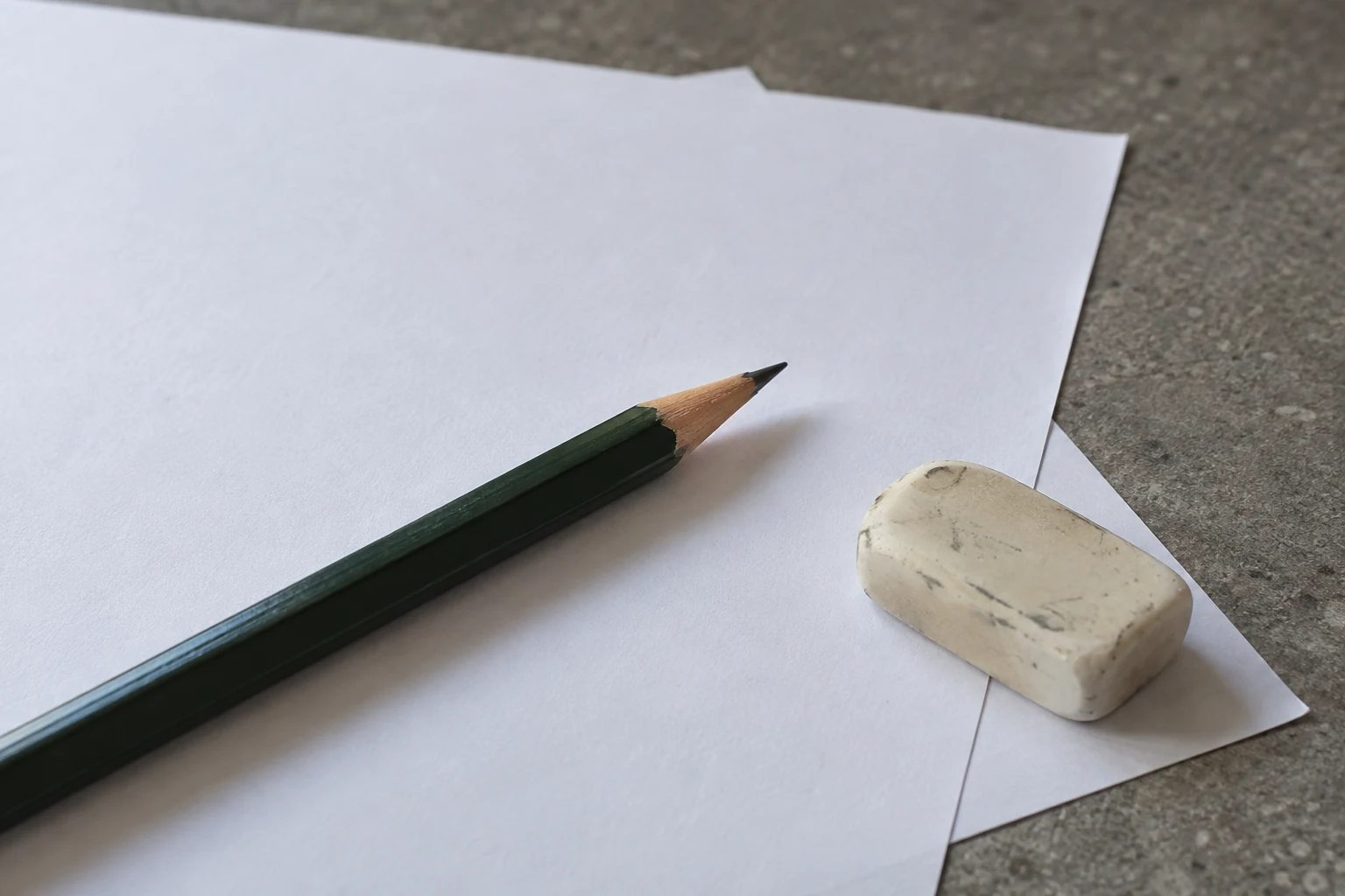 Groen potlood en een gebruikte gum op onbeschreven vellen papier.