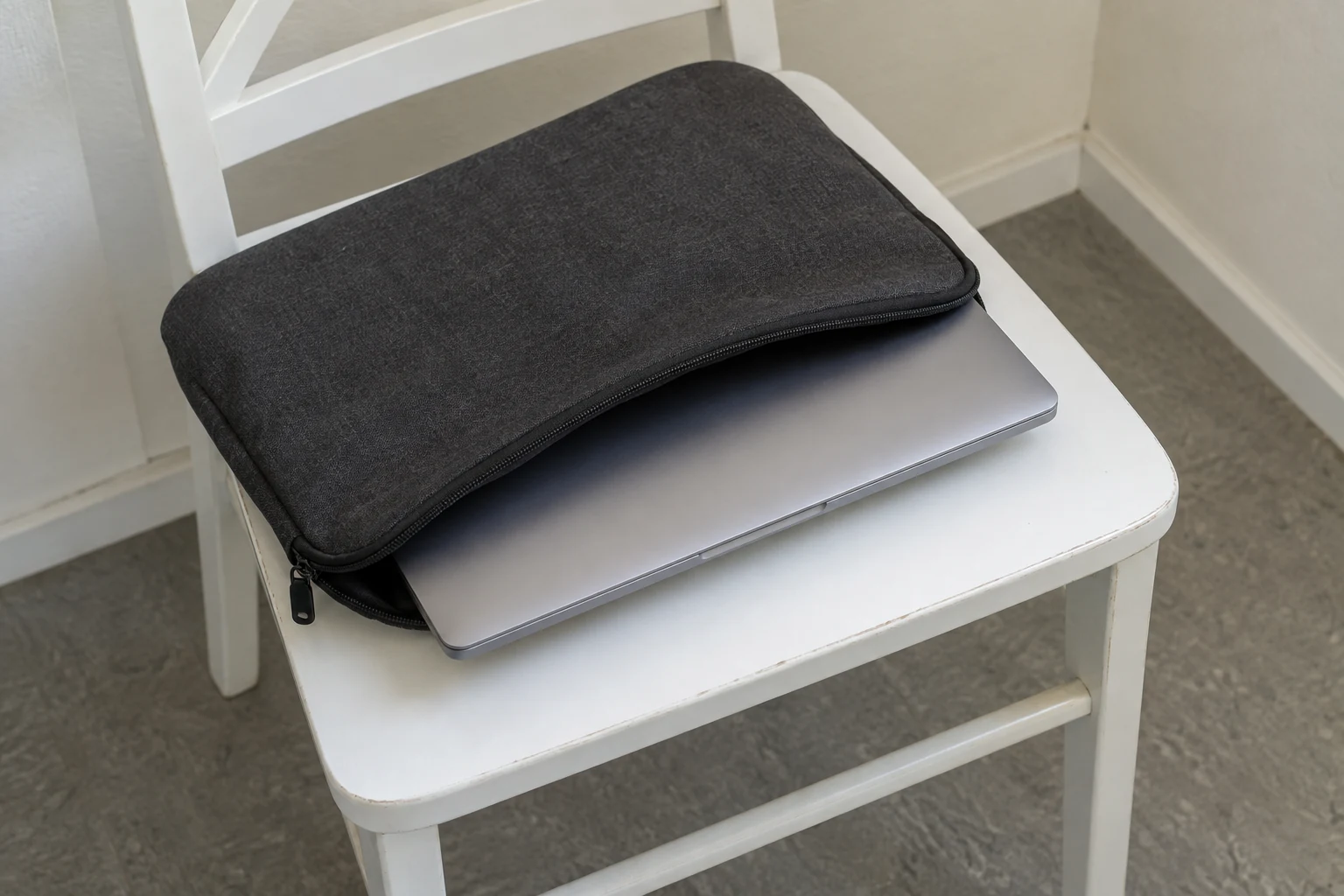 Gesloten laptop steekt gedeeltelijk uit een stoffen hoes op een witte stoel.