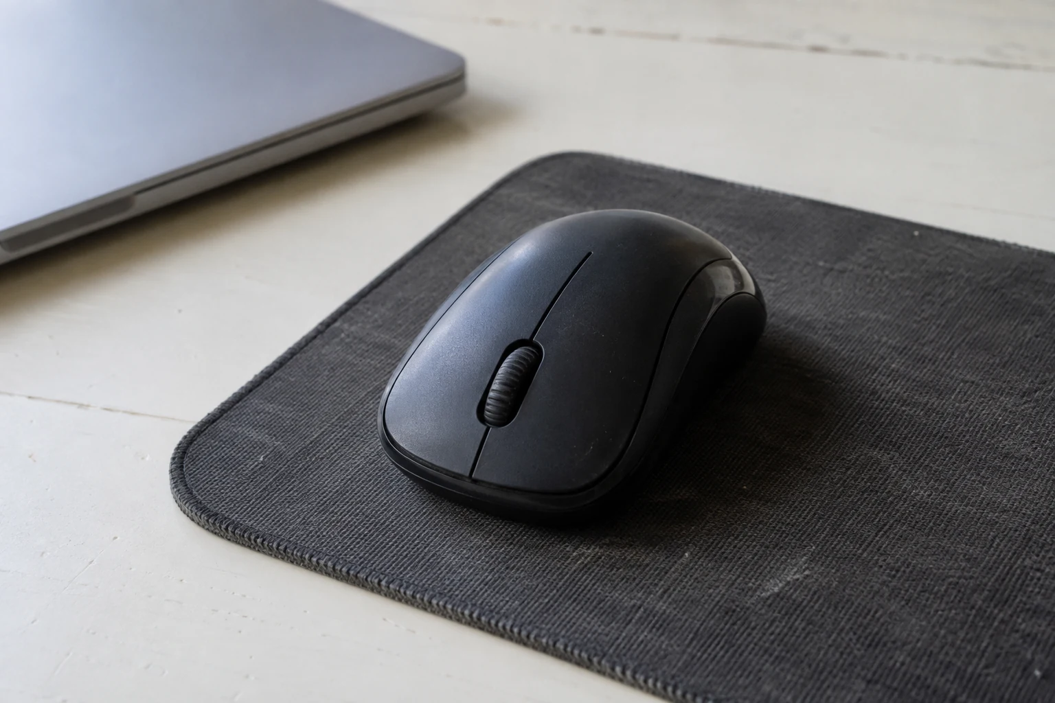 Zwarte computermuis op een stoffen muismat naast de hoek van een gesloten laptop.
