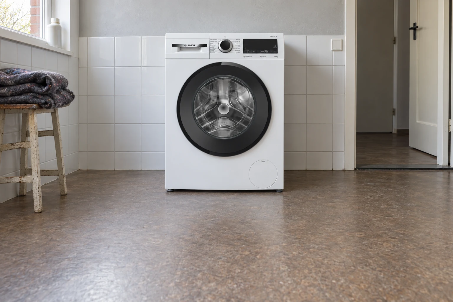 Witte wasmachine in een eenvoudige bijkeuken met vrije ruimte ervoor.