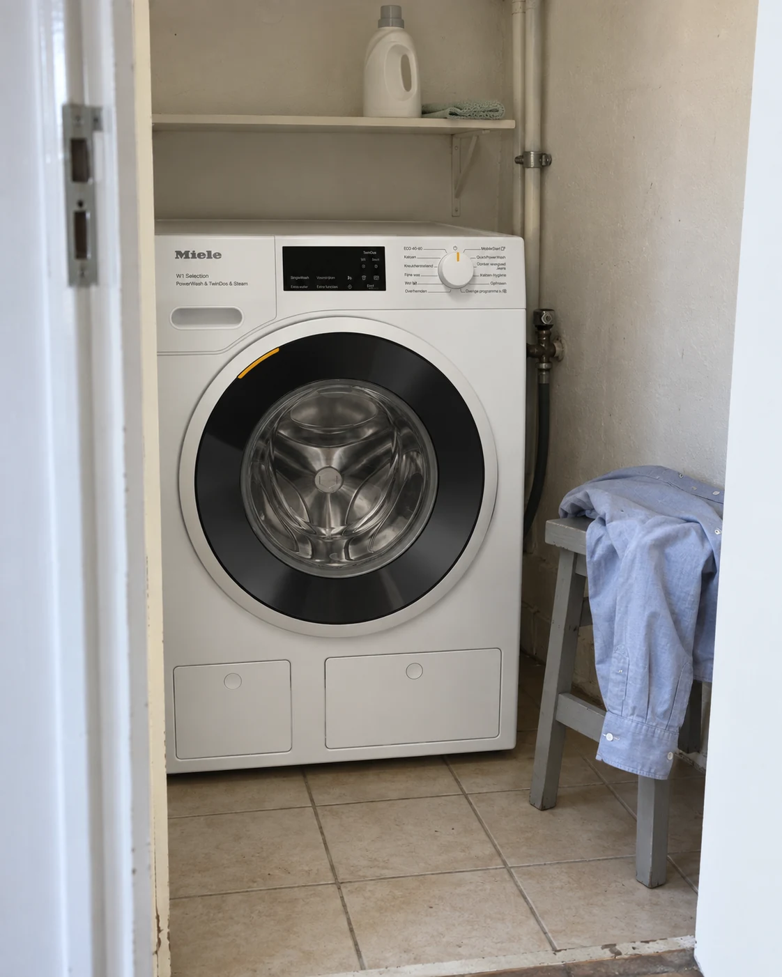 Een los overhemd ligt op een kruk naast een Miele-wasmachine