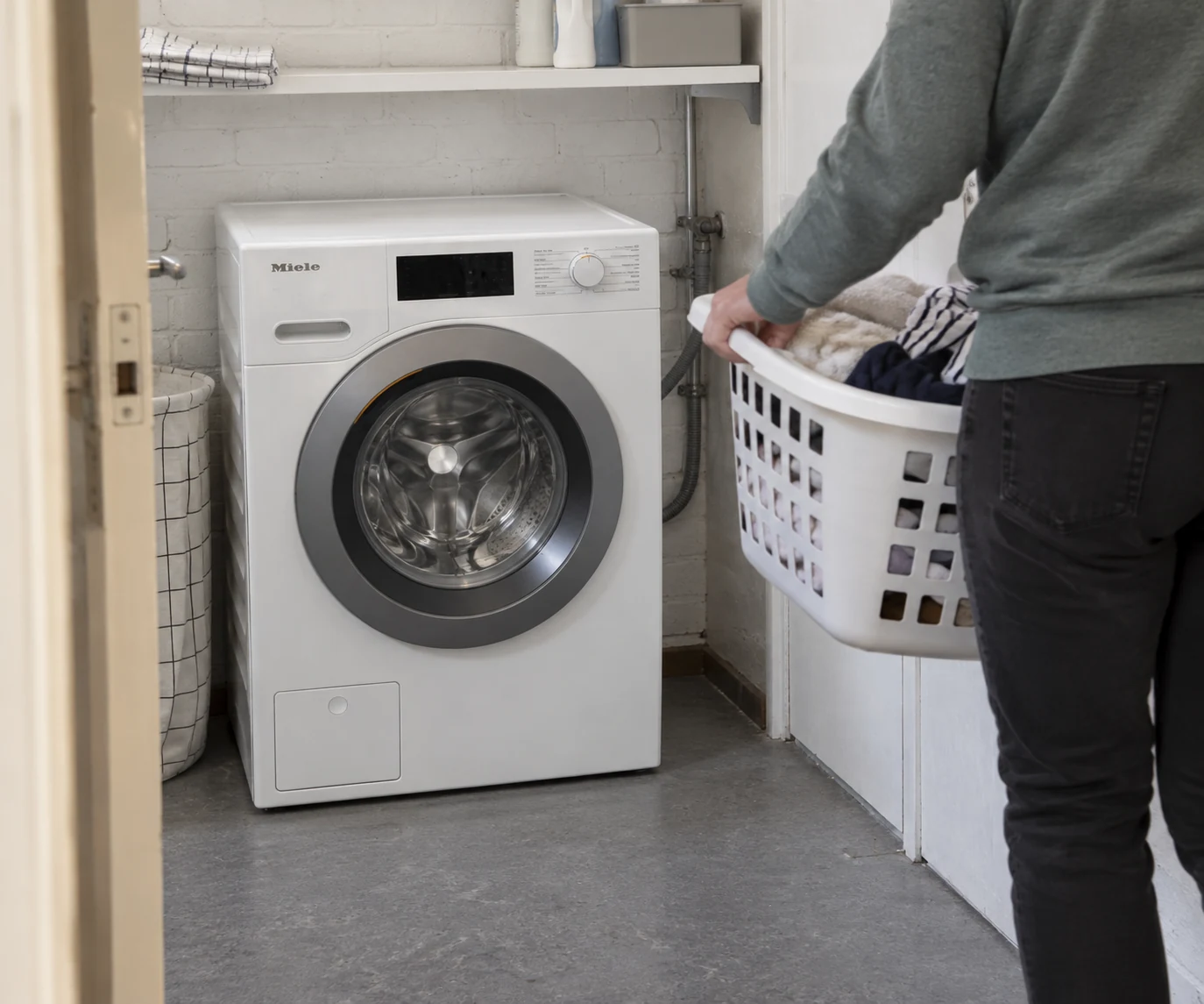 Miele-wasmachine in een wasruimte naast iemand met een wasmand