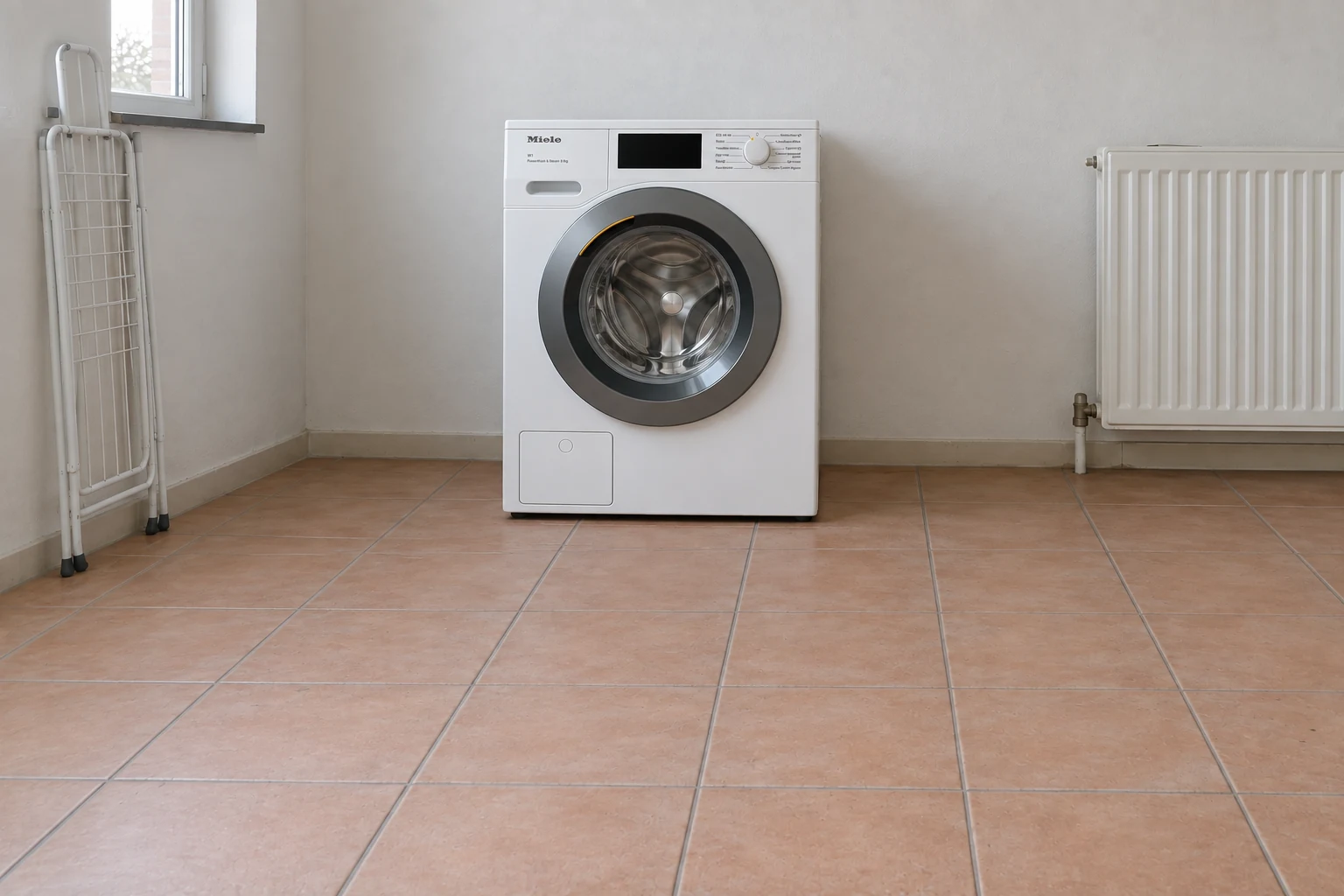 Miele WEC 388 in een eenvoudige washoek met een lichtbruine tegelvloer.