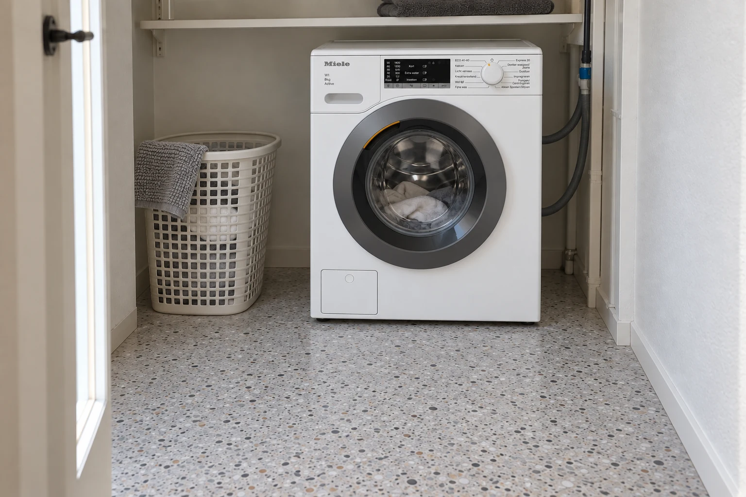 Witte Miele wasmachine in een smalle washoek met een wasmand en lichte vloer.