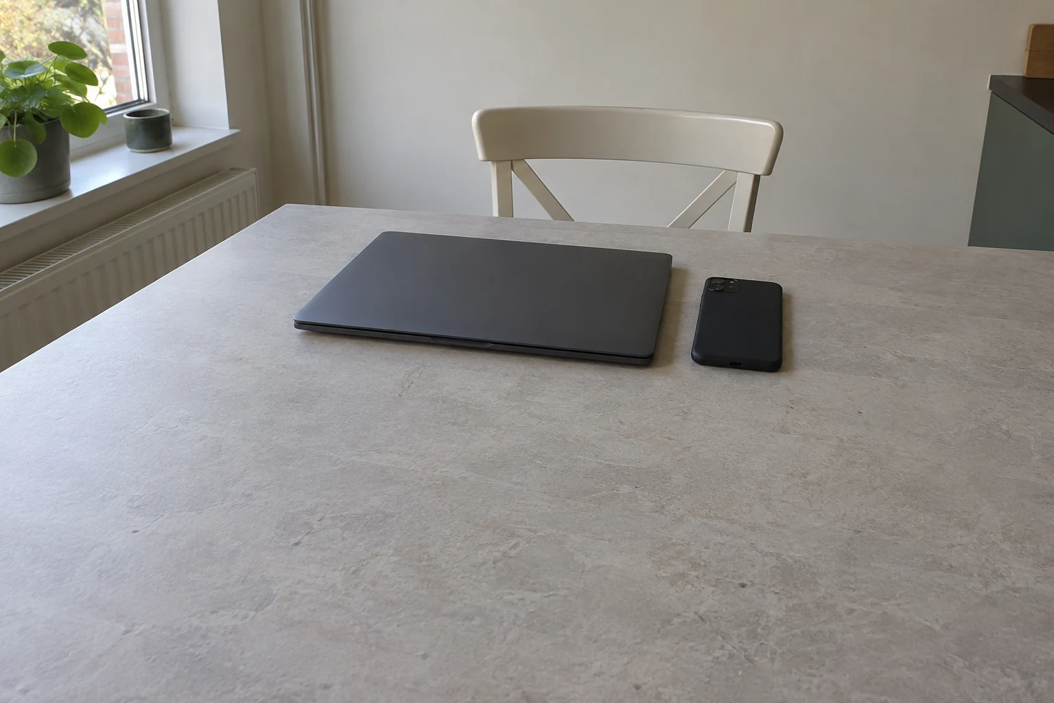 Gesloten laptop en omgekeerde telefoon op een lichte keukentafel.