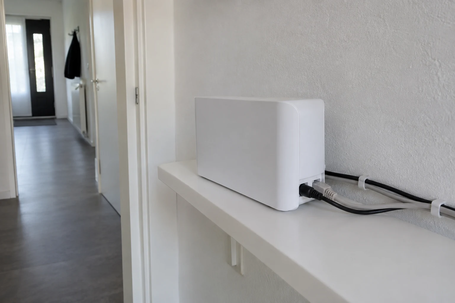 Witte thuisrouter op een wandplank met twee langs de muur geleide kabels.