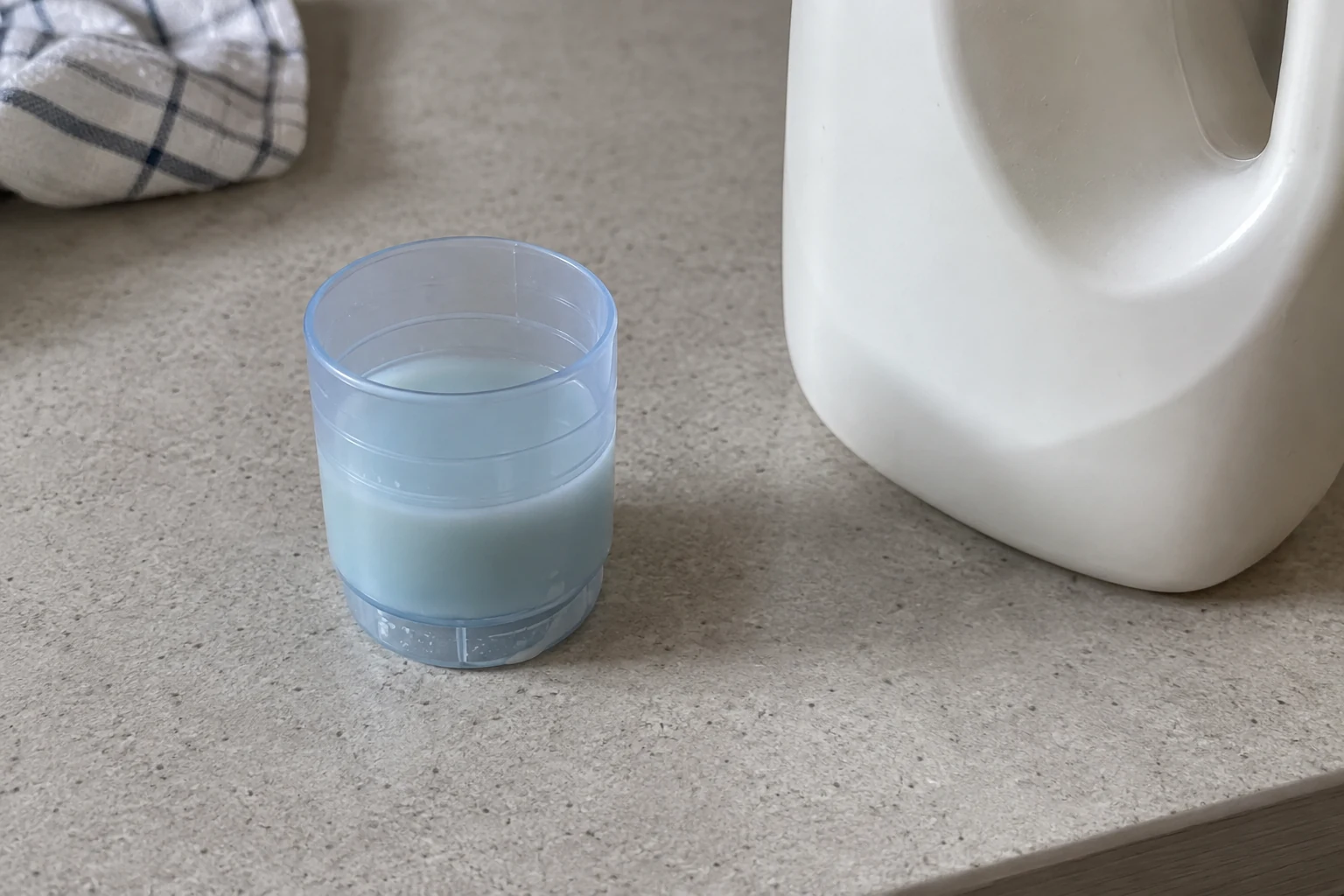 Een doseerdop met vloeibaar wasmiddel naast een fles op een wasblad