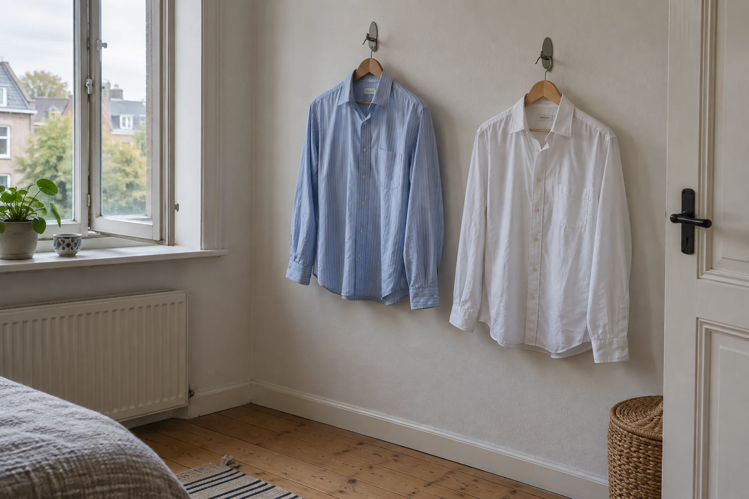 Twee licht gekreukte katoenen overhemden aan hangers bij een open raam