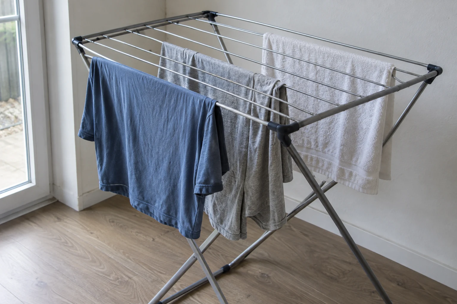 Katoenen kleding hangt met ruimte ertussen op een wasrek bij het raam