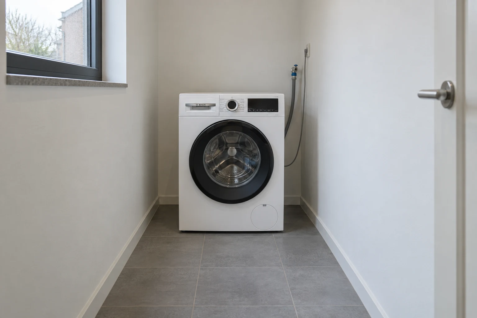Een moderne Bosch-wasmachine staat aan het einde van een smalle wasruimte.