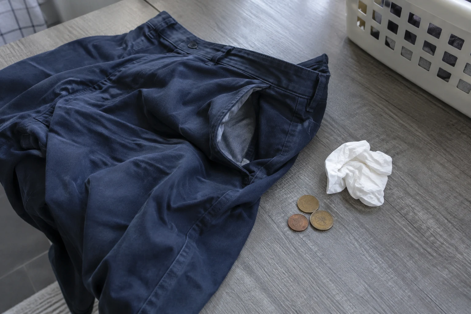 Een broek met open zak ligt naast enkele muntjes en een papieren zakdoekje.