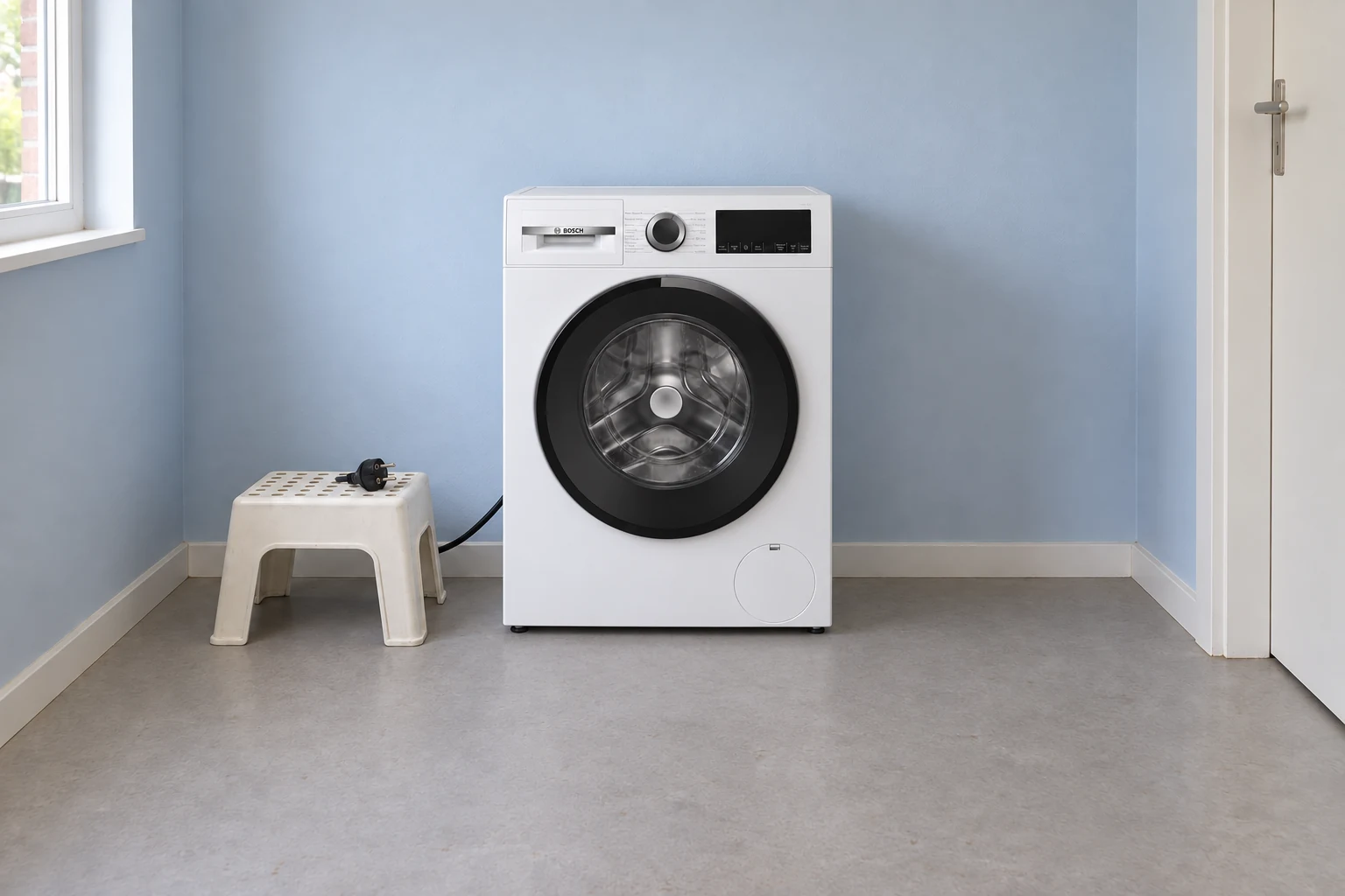 Een witte wasmachine in een eenvoudige wasruimte met een losse stekker op een bankje ernaast.