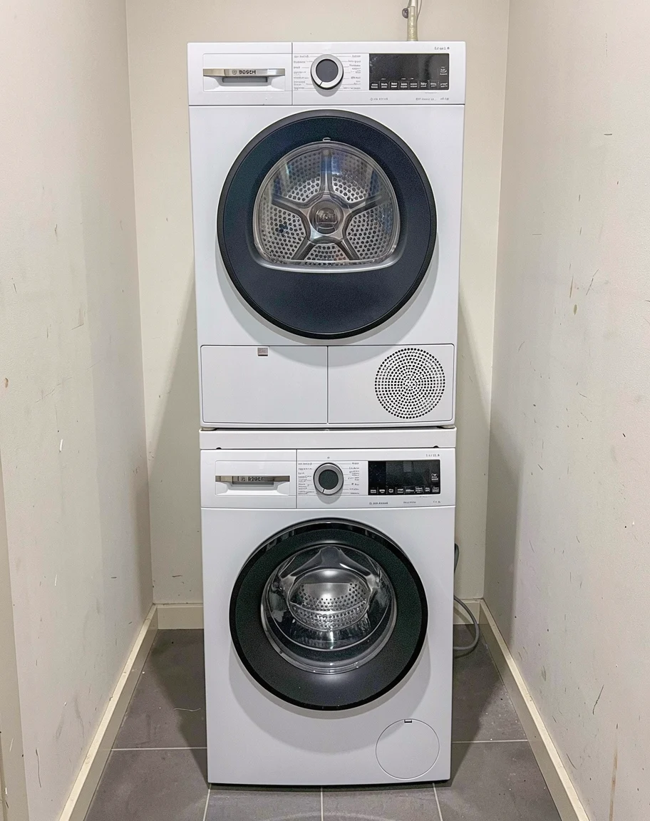Bosch-droger boven een Bosch-wasmachine, gestapeld met een witte verbindingsset in een wasruimte