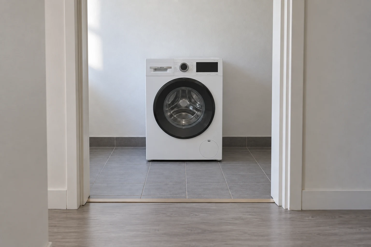 Een witte wasmachine is door een open binnendeur zichtbaar in een compacte wasruimte.