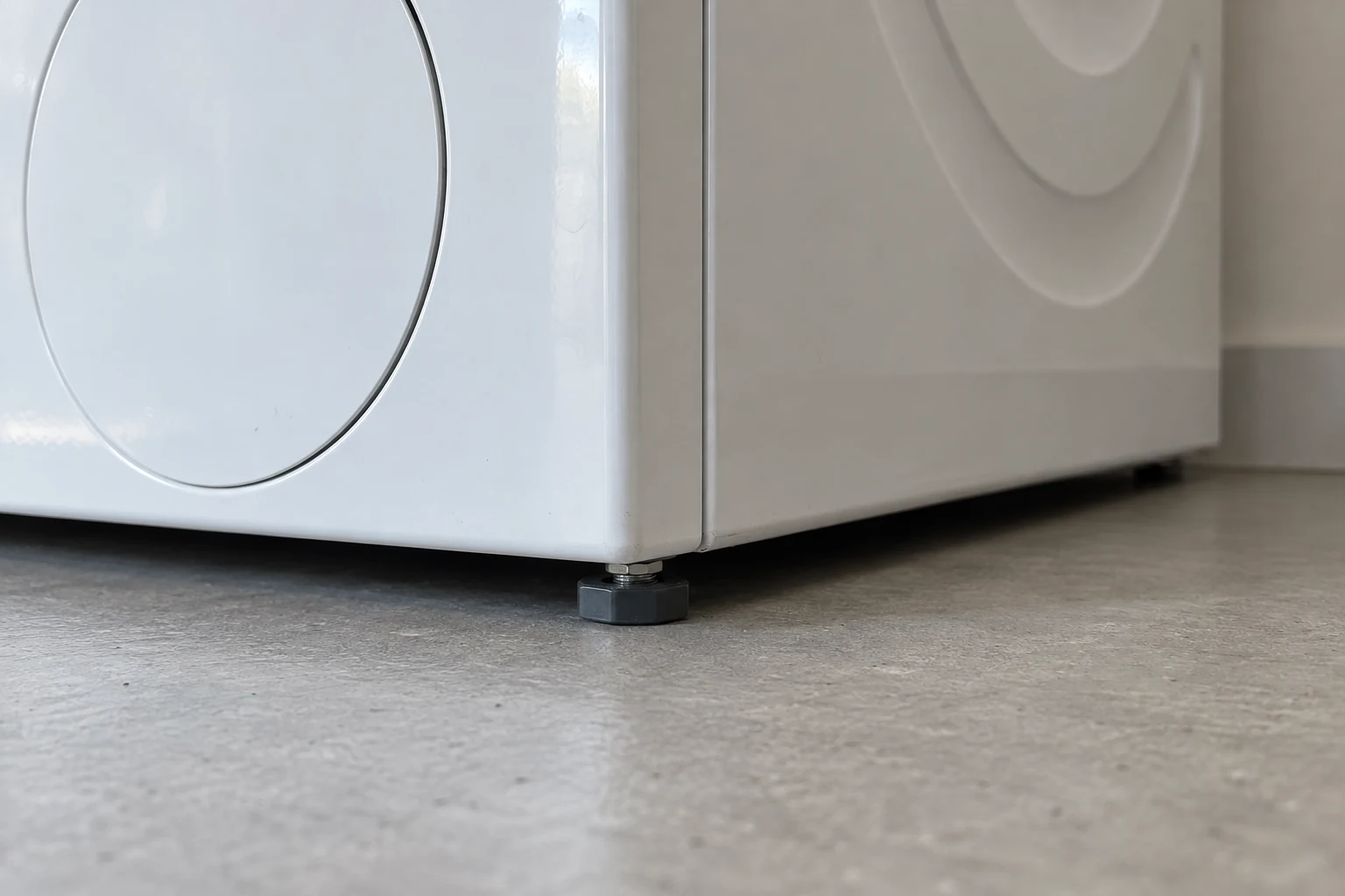Een kort stelvoetje onder de hoek van een wasmachine rust op een harde vloer.
