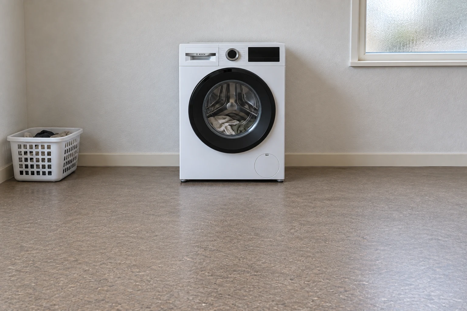 Witte wasmachine met gesloten deur in een eenvoudige washoek.