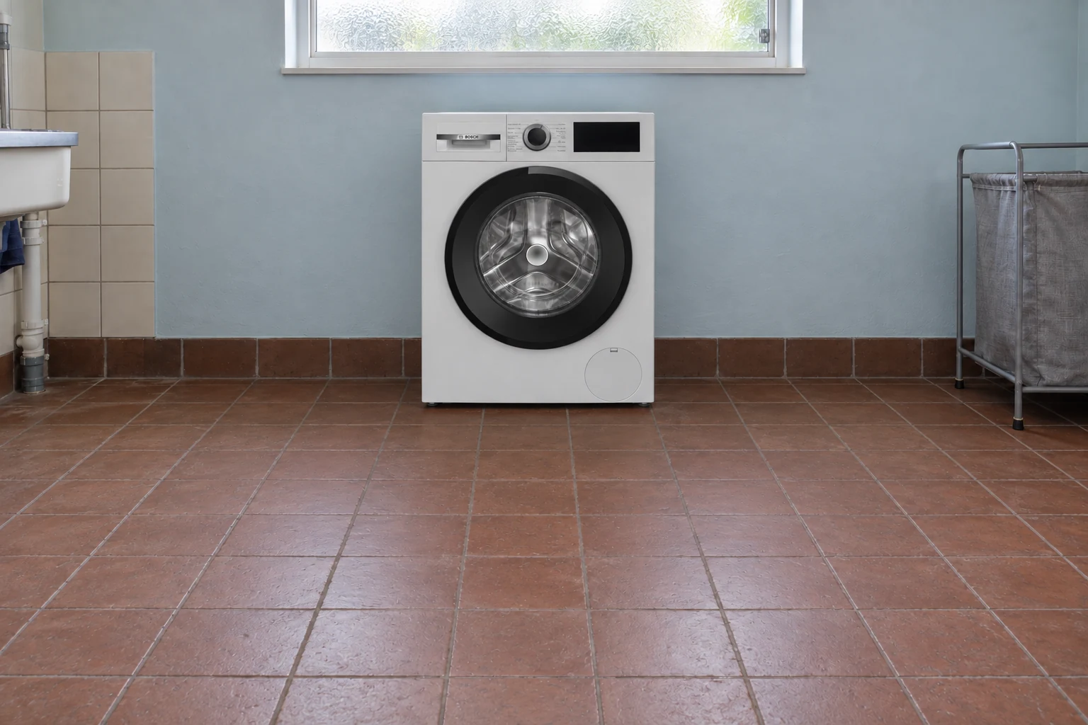 Witte wasmachine op een bruinrode tegelvloer in een eenvoudige bijkeuken.