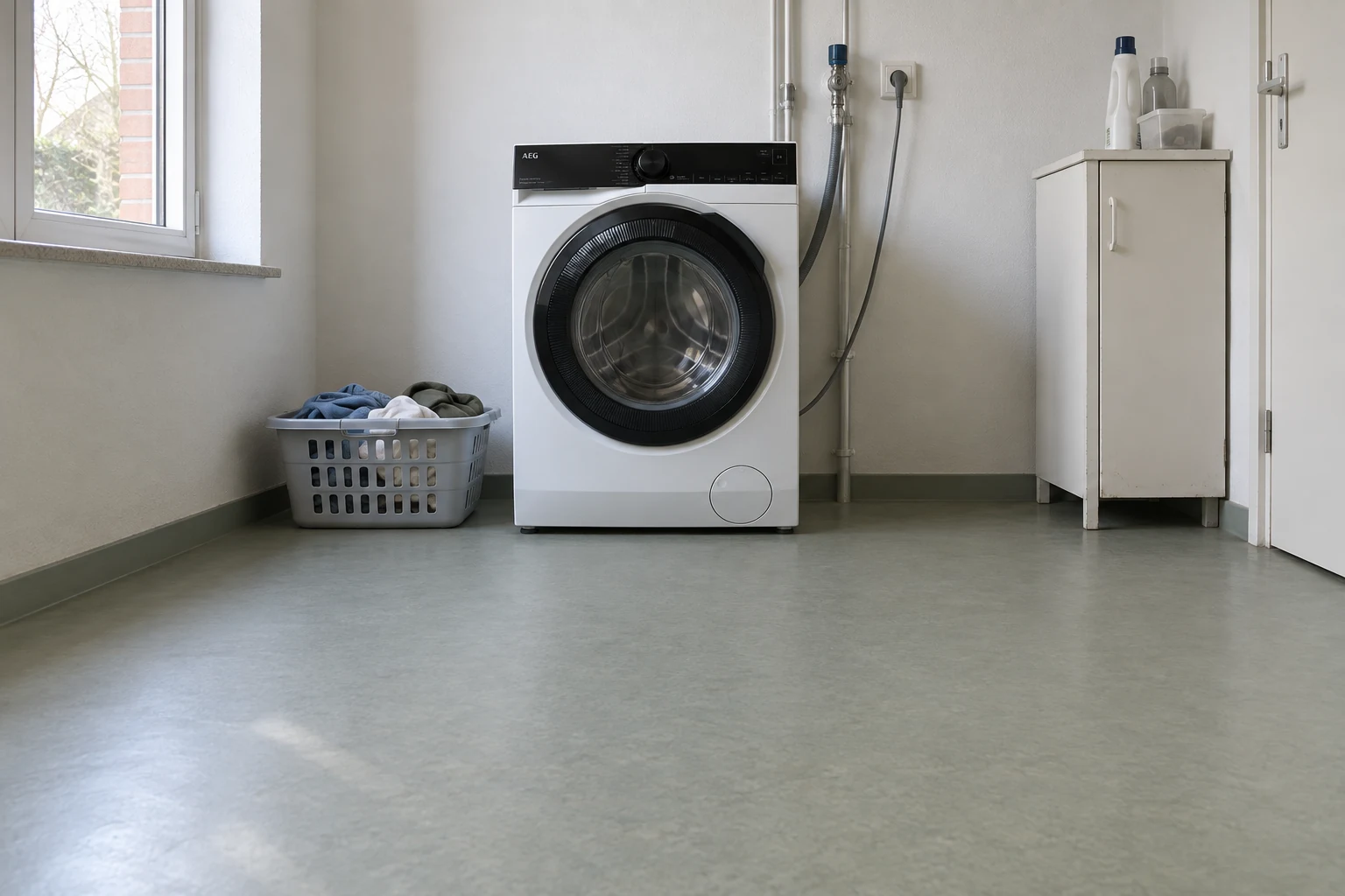 Een witte wasmachine met gesloten deur in een praktische wasruimte, met een kleine kledingmand ernaast.