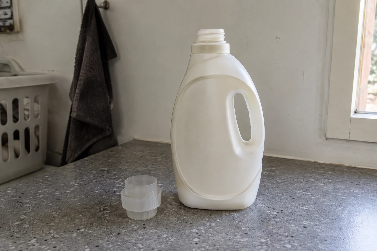 Een gewone wasmiddelfles staat naast een lege maatdop op een gebruikt werkblad.